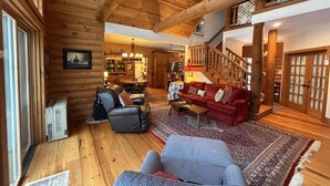 A log cabin interior with a dining area, a living room with a red sofa, and a staircase leading to an upper level.