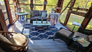 A wooden deck with wicker furniture, a blue patterned rug, and a table with decorative items.