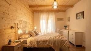 Une chambre à coucher aux murs lambrissés, comprenant un lit, des lampes de chevet, une table de chevet, une commode et un luminaire suspendu.