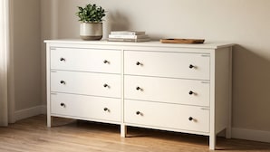 Une commode blanche à six tiroirs, chacun étant étiqueté « PRIVATO ». Une plante en pot et une pile de livres sont posées sur le dessus.