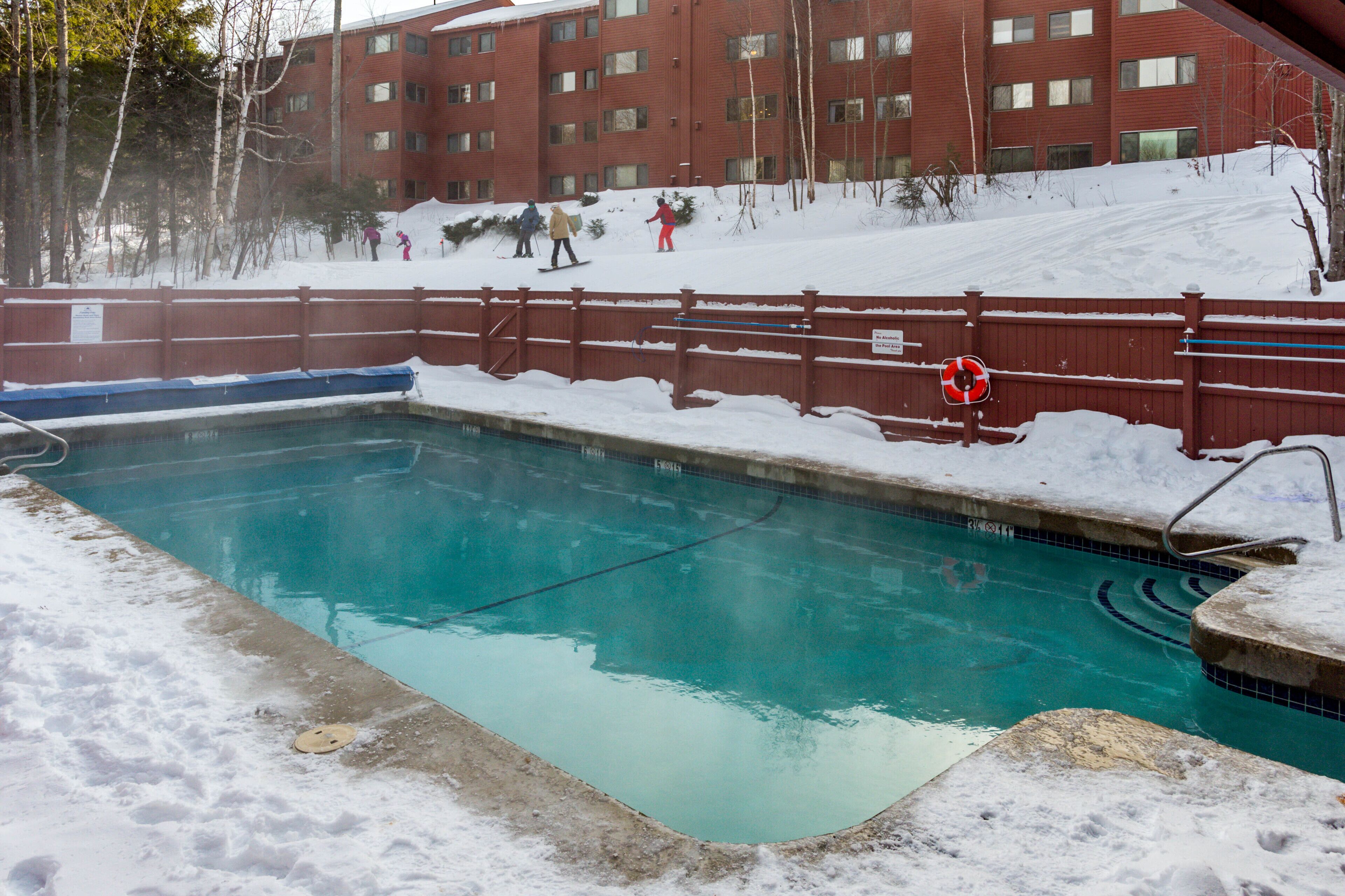 Una piscina rodeada de nieve, con un edificio rojo al fondo.