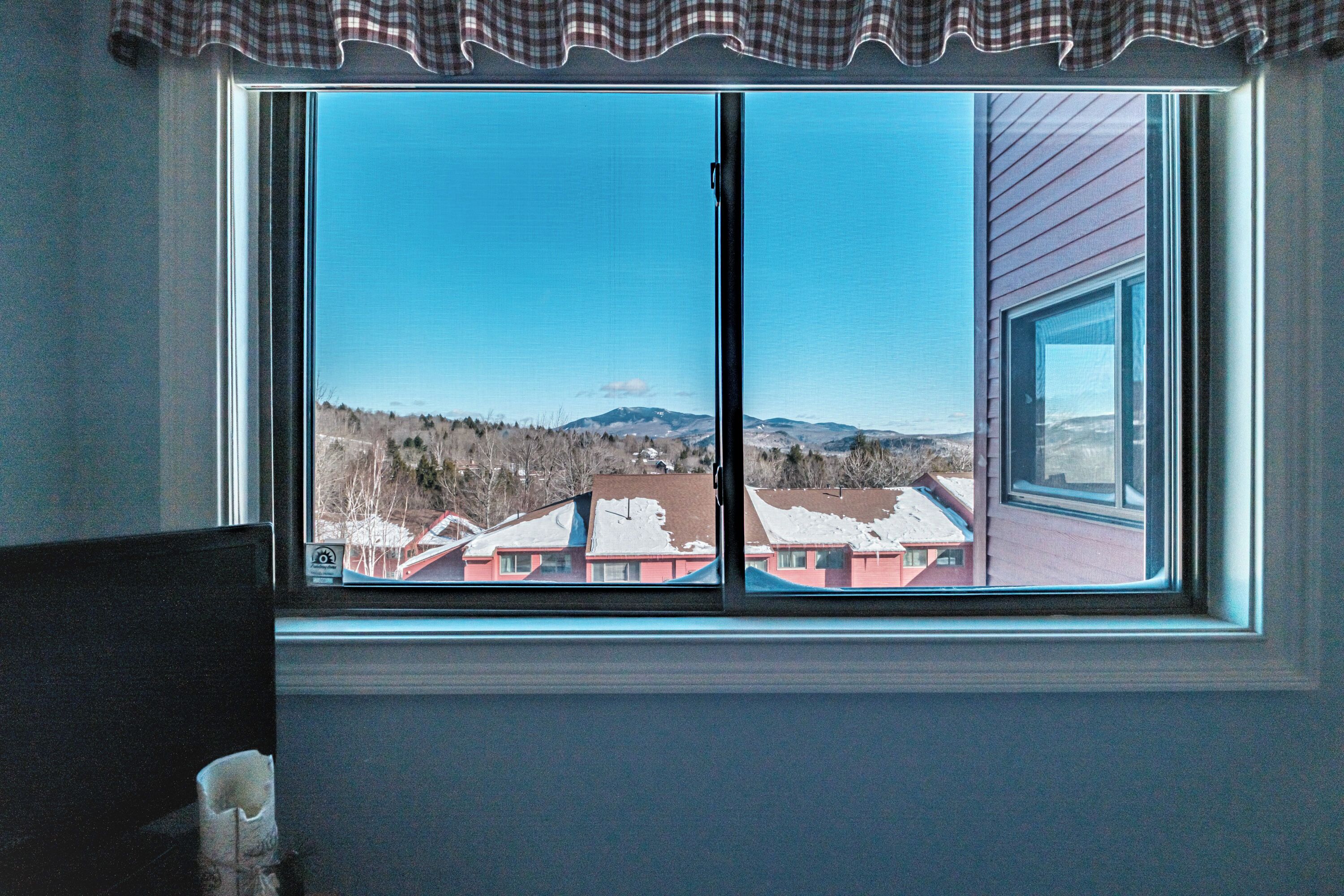 A room with a large window offering a view of a residential area and mountains.