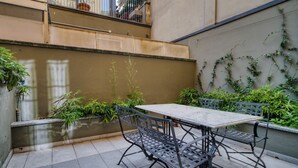 Een terras met een tafel en stoelen, omringd door planten en een muur begroeid met klimop.