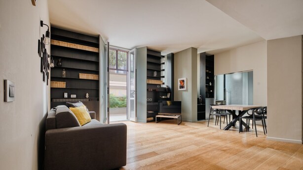 Een moderne woonkamer met een bank, een eettafel en een inbouwboekenplank.