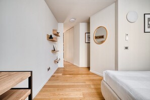 A hallway with wooden flooring, a bed, a round mirror, and wooden shelves. - Hostmate - Milano - Solari (Milan)