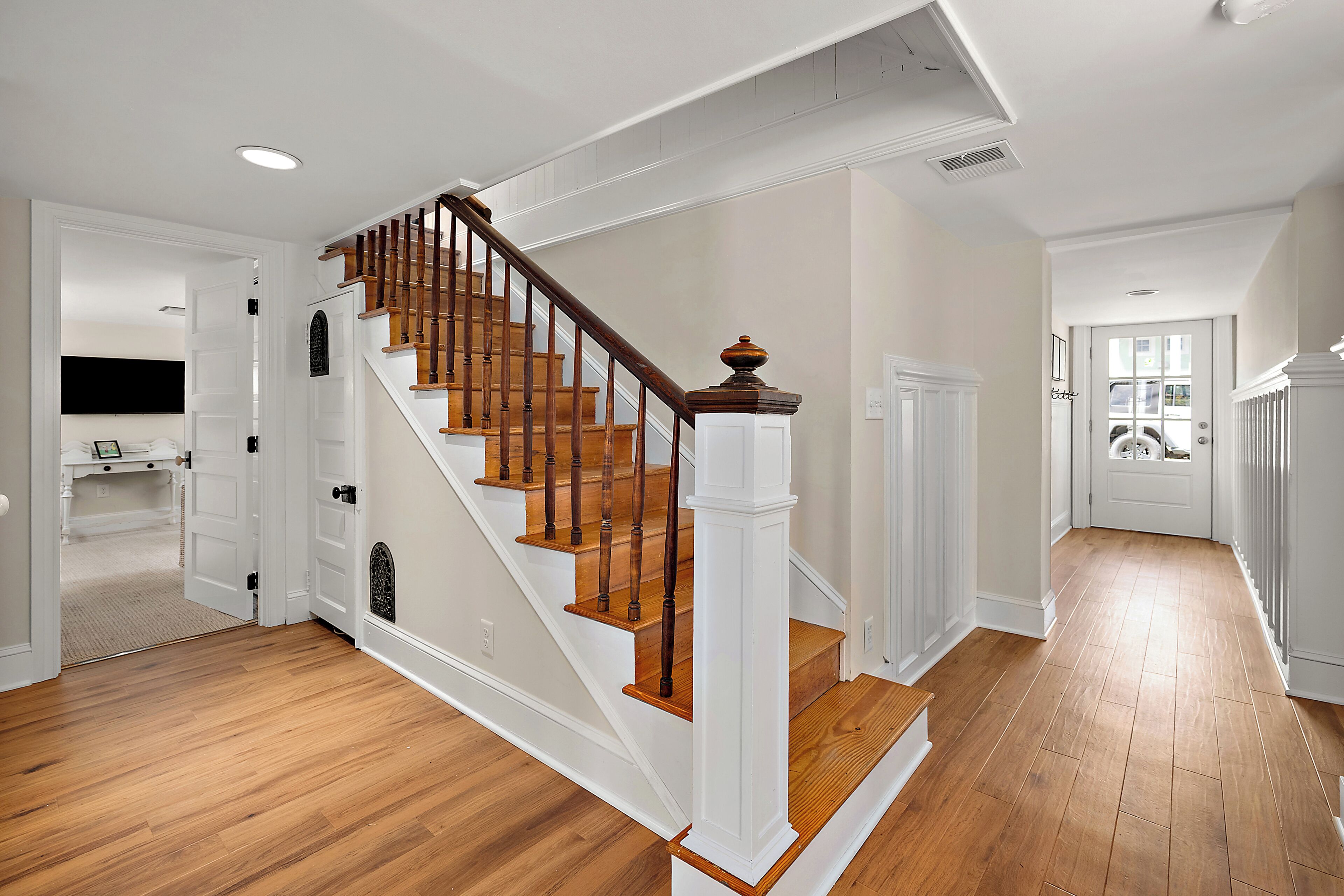 A staircase with wooden steps and white railings, leading to a room with a white door and a window.