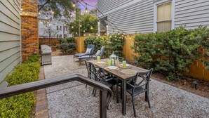 En terrasse med et bord dækket til fire personer, omgivet af stole, en lanterne og en grill.