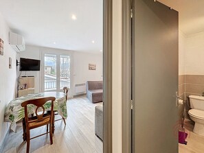 Una habitación con cama, televisor, mesa con sillas, sofá y baño con inodoro y ducha.