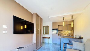 A modern hotel room with a flat-screen TV mounted on the wall, a small dining area with a bar, and a seating area with a sofa and a chair. - Renovated Apartment with Terrace and Parking in Menton (Menton)