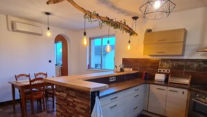 A kitchen with a central island, wooden chairs, a dining table, and a hanging light fixture. - Renovated eco-village cottage, air-conditioned, pet-friendly (Ville-sur-Yron)