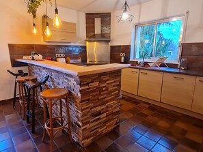 Een moderne keuken met een centraal kookeiland, barkrukken, een raam met uitzicht en hangende pendantlampen.