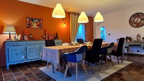 A dining area with a table set for four, blue chairs, a blue cabinet, and a clock on the wall. - Renovated eco-village cottage, air-conditioned, pet-friendly (Ville-sur-Yron)
