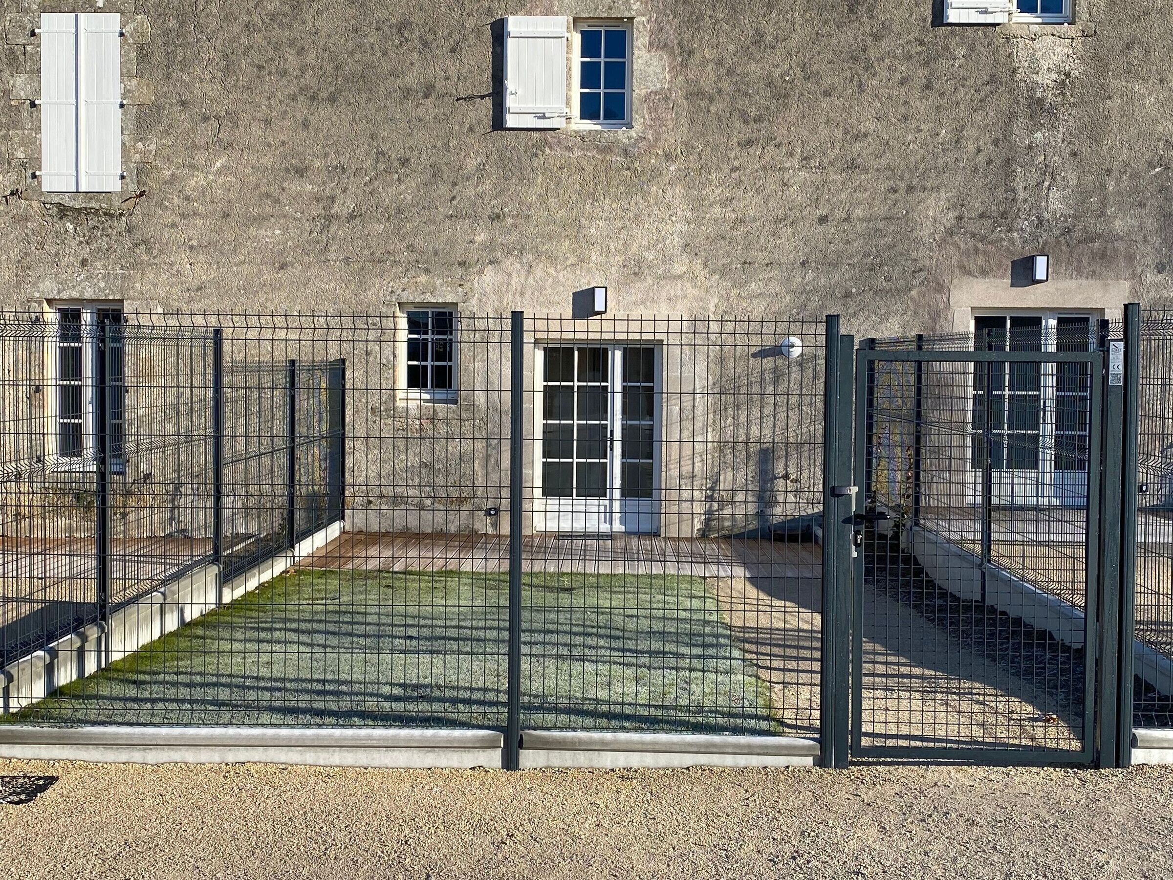 Een gebouw met een gevel van natuursteen, meerdere ramen en een omheind binnenterrein.
