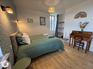 A bedroom with a bed, a desk, and a chair. There are two wall-mounted lights, a window, and a wall decoration. - Charming Cottage in Vendée with Private Parking (La Gaubretière)