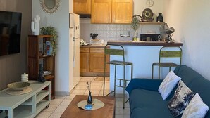 A compact living space with a kitchenette, a TV mounted on the wall, a blue sofa, and a small coffee table. - Air-Conditioned Apartment with Parking in Saint-Gilles (Saint-Gilles les Bains)