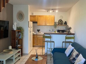 A compact living space with a kitchenette, a TV mounted on the wall, a blue sofa, and a small coffee table. - Air-Conditioned Apartment with Parking in Saint-Gilles (Saint-Gilles les Bains)