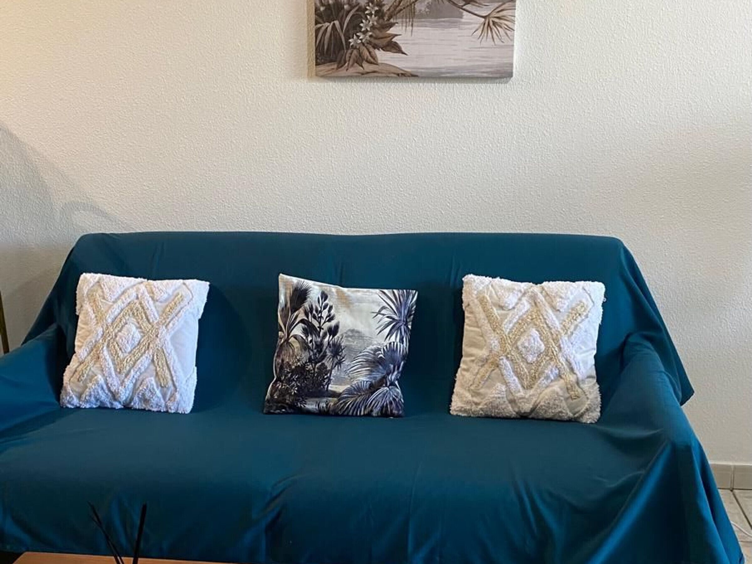 En turkis sofa med tre dekorative puder, et indrammet kunstværk over og et træbord med et lys.