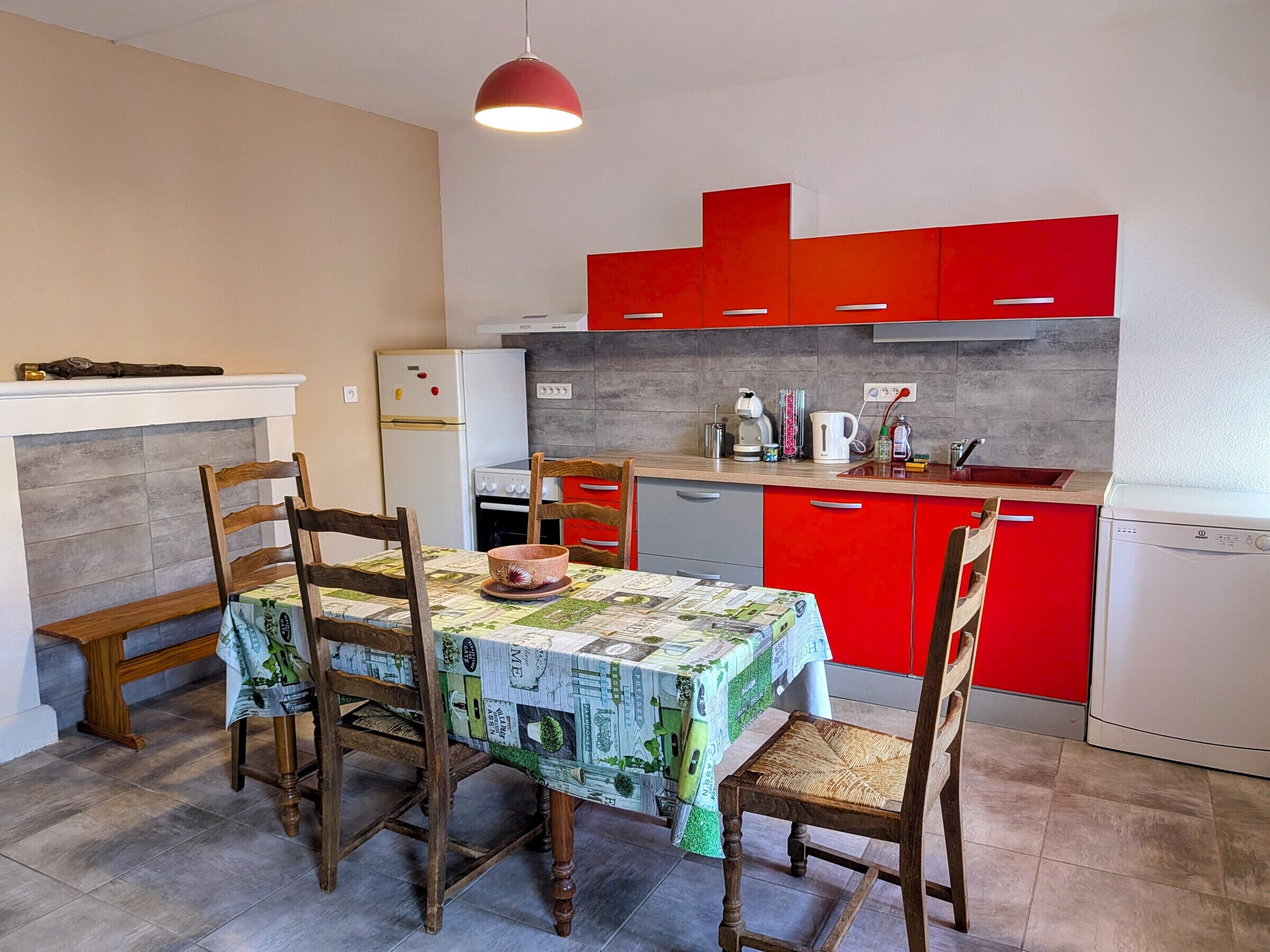 Una cocina compacta con armarios rojos, un refrigerador blanco y una mesa de comedor con cuatro sillas.
