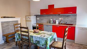 Una cocina compacta con armarios rojos, un refrigerador blanco y una mesa de comedor con cuatro sillas.