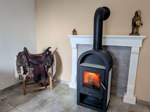 A fireplace with a black wood-burning stove, a white mantel, and a saddle with leather straps on a wooden stand.