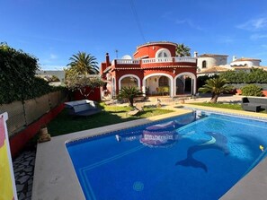 Ein Pool mit Delphin-Motiv, ein rotes Gebäude mit Bögen und ein klarer, blauer Himmel.