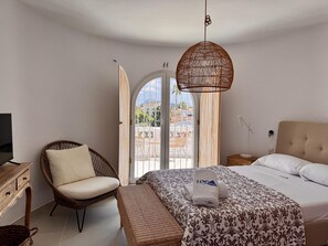 Ein Schlafzimmer mit Bett, Sessel, Fernseher, Nachttisch und Blick durch eine offene Tür.