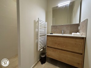 A bathroom with a white radiator, a mirror above a sink, and a trash bin. - Charming Vendée Cottage with Garden - 6 Guests (La Gaubretière)