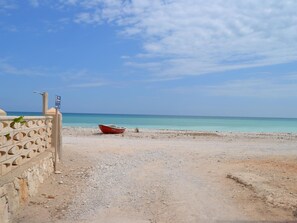 Ein Strand mit einem Boot, einer Steinmauer und einem wolkenlosen Himmel.