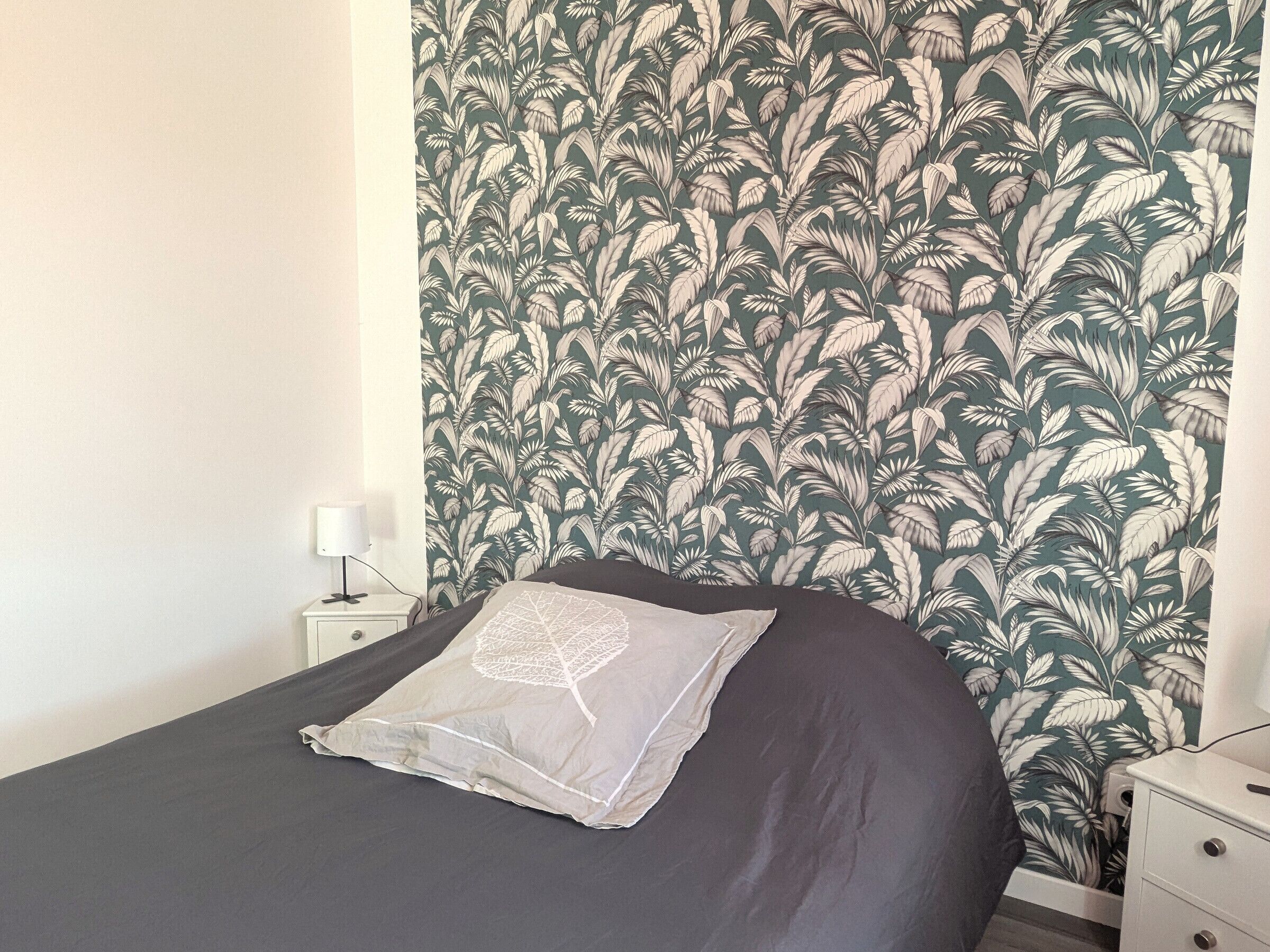 A bedroom with a bed, a nightstand, and a wall with a leafy pattern.