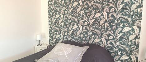 A bedroom with a bed, a nightstand, and a wall with a leafy pattern.