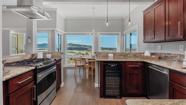 A modern kitchen with a stove, oven, dishwasher, and a view of the outdoors. - Surf & Saddle - Racetrack, Ocean Views from this Gorgeous Condo with AC (Solana Beach)
