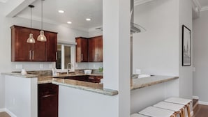 A modern kitchen with dark wood cabinets, granite countertops, and pendant lighting. - Surf & Saddle - Racetrack, Ocean Views from this Gorgeous Condo with AC (Solana Beach)