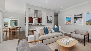 A modern living room with a sofa, armchairs, a coffee table, and a dining area with a table and chairs. - Surf & Saddle - Racetrack, Ocean Views from this Gorgeous Condo with AC (Solana Beach)