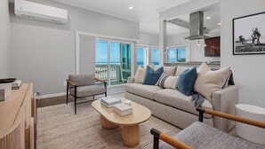 A modern living room with a sofa, armchairs, a coffee table, and a view of the sea through large windows. - Surf & Saddle - Racetrack, Ocean Views from this Gorgeous Condo with AC (Solana Beach)