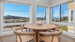 A dining area with a round table and chairs, large windows with a view of a landscape, and a white chandelier. - Surf & Saddle - Racetrack, Ocean Views from this Gorgeous Condo with AC (Solana Beach)