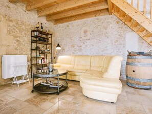 A cozy living room with a stone wall, a wooden ceiling, a beige sofa, a small round table, and a bookshelf.