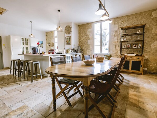 A spacious kitchen with a large wooden table and bar stools, stone walls, and a rustic wooden cabinet with shelves.
