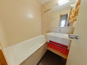 A bathroom with a white bathtub, a sink with a mirror above it, and a wooden shelf with red storage drawers. - Cozy apartment with loggia in the heart of Jura (Prémanon)
