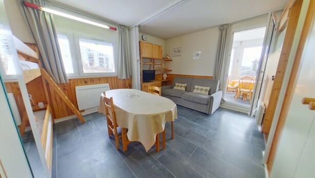 Ein Zimmer mit Esstisch, einer Couch, einem Fernseher und einem Fenster.