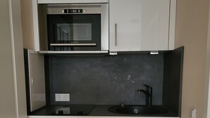 Una cucina compatta con forno integrato e microonde, lavello e un piano di lavoro con bollitore.