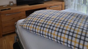 Una camera da letto con un letto, una televisione su una cassettiera di legno e una finestra con tende decorate.