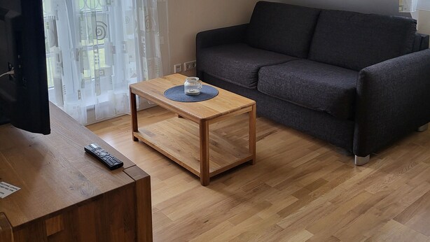 Un soggiorno con un tavolino in legno, un divano grigio scuro e una televisione su un mobile in legno.