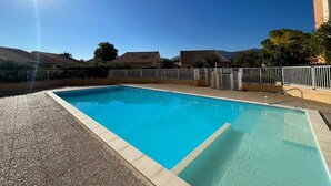 A rectangular swimming pool with clear blue water, surrounded by a gravel area and a white metal fence. - 2-Bedroom Pavilion with Parking in Argelès-sur-Mer (Argelès-sur-Mer)