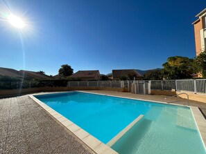 A rectangular swimming pool with clear blue water, surrounded by a gravel area and a white metal fence. - 2-Bedroom Pavilion with Parking in Argelès-sur-Mer (Argelès-sur-Mer)