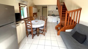 A compact kitchen with a dining table, chairs, a sofa, and a wooden staircase. - 2-Bedroom Pavilion with Parking in Argelès-sur-Mer (Argelès-sur-Mer)