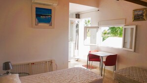 Camera da letto con due letti, un tavolino e una sedia. Una finestra offre vista sul verde circostante.