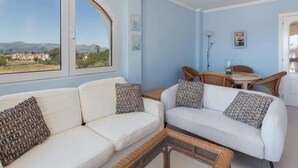 A modern living room with a white sofa set, a dining area with wicker chairs, and a large window offering a scenic view. - Charming 2-Bedroom Apartment in Denia, Beach Access, Parking Included (Denia)