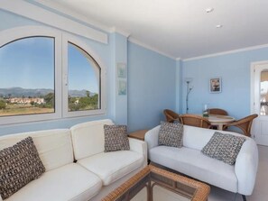 Ein modernes Wohnzimmer mit einer weißen Sofagarnitur, einem Essbereich mit Korbstühlen und einem großen Fenster mit Panoramablick.