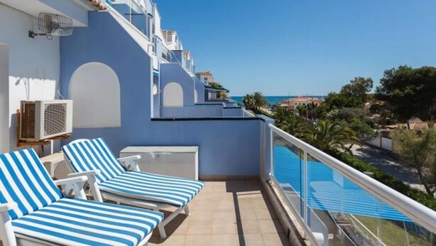 A balcony with blue-striped lounge chairs, a pool, and a clear view of the sea. - Charming 2-Bedroom Apartment in Denia, Beach Access, Parking Included (Denia)