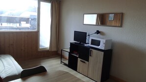 A room with a bed, a desk with a computer and a microwave, a window with a view of buildings, and a mirror on the wall. - Studio in Station Center with Free Wi-Fi (Besse-et-Saint-Anastaise-Super Besse)